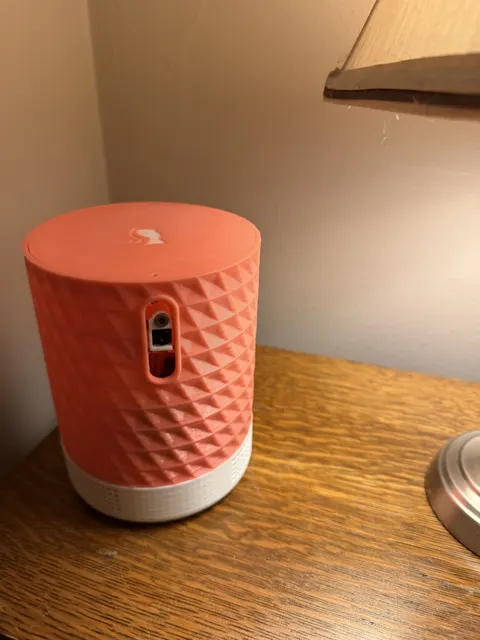 CatZoom on a nightstand: a coral faceted printed shade on a white base, the laser and camera behind a slot in the side