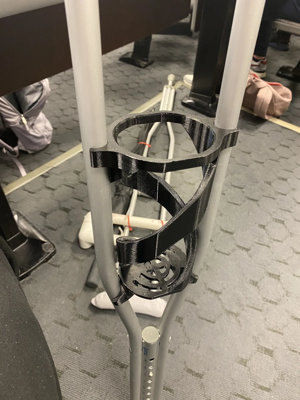 Black printed helical holder clamped between the rails of an aluminum crutch in a lecture hall